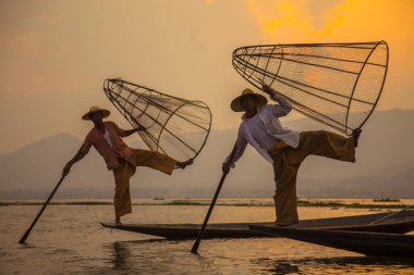 Inle Lake, Myanmar - Spring, 2018: two traditional fishermen of Lake Inle Lake lifting the net and holding it with the feet 