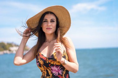 Yazlık elbise ve kumsalda hasır şapka giyen güzel bir kadın.