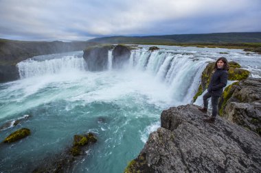 Godafoss şelalesi, şelalenin tepesinde genç bir turist. İzlanda