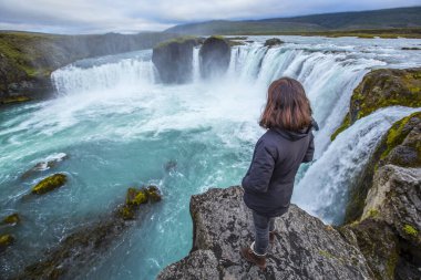 Godafoss şelalesi, şelalenin üstünde genç bir kadın. İzlanda