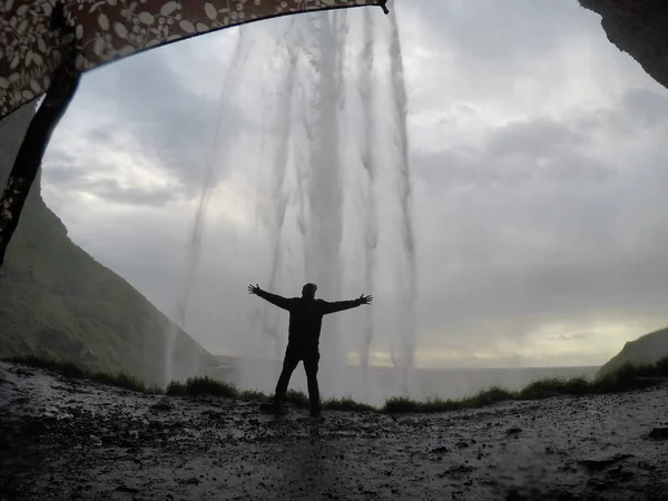 A young man with open arms behind Seljalandsfoss waterfall in beautiful Iceland