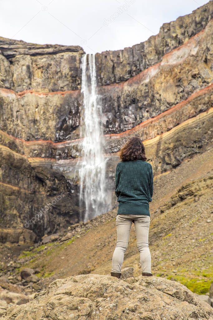 A young woman looking at Hengifoss waterfall, the third tallest waterfall in Iceland