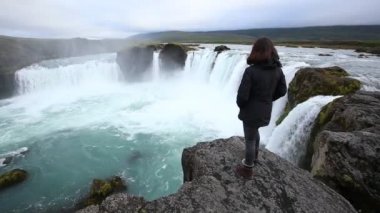 Yukarıdan Godafoss şelalesine bakan genç bir kadın. İzlanda