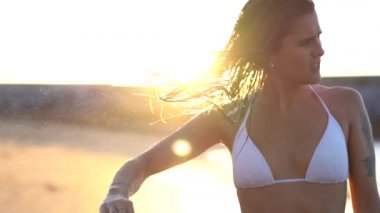 Yaşam tarzı, genç esmer beyaz bir kadın gün batımında kumsalda saçlarını kurutuyor.