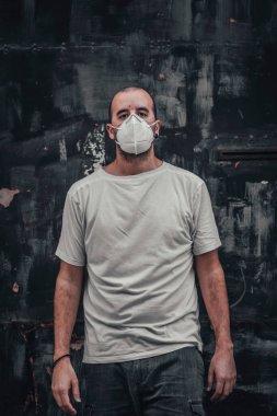 Siyah metal bir kapıda beyaz gömlekli ve maskeli genç bir adam. Sağlık acil durumu, salgın Covid-19