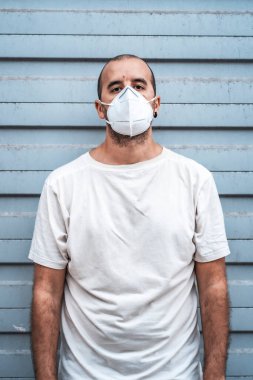 Metal bir kapıda beyaz gömlekli ve maskeli genç bir adam. Sağlık acil durumu, salgın Covid-19