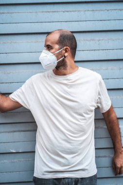 Metal kapısında maskesi olan genç bir adam sola bakıyor. Sağlık acil durumu, salgın Covid-19
