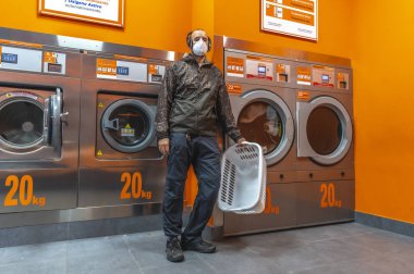 Çamaşırhanede bekleyen Coperid-19 maskeli genç bir adam. Sosyal mesafe, koronavirüs salgını