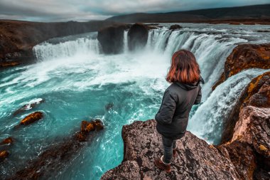 Yukarıdan Godafoss şelalesine bakan genç bir turist. İzlanda