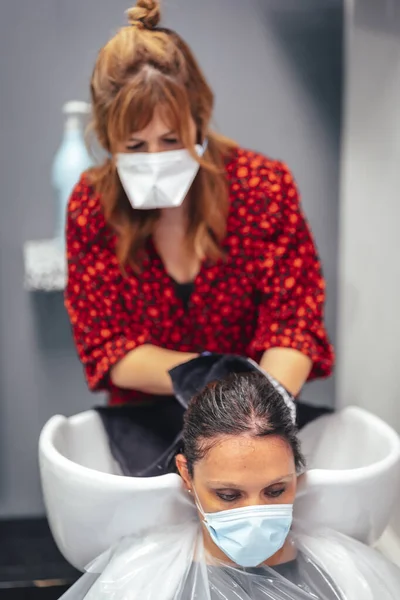 Hairdresser with mask and gloves washing the client\'s hair with soap and water. Reopening with security measures for hairdressers in the Covid-19 pandemic