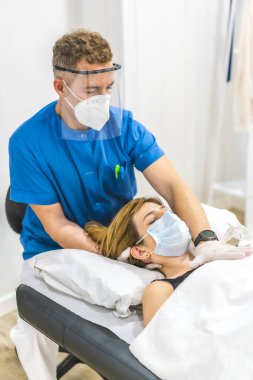 Sedyedeki bir hasta için koruyucu önlemler alan bir fizyoterapistin yapısal osteopatisi. Covid-19 salgını. Osteopati, tedavi edici kiromasaj.