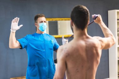 Fizyoterapistle kol egzersizi yapan bir hasta. Koronavirüs salgını için koruyucu önlemlerle fizik tedavi, COVID-19. Osteopati, tedavi edici kiromasaj.