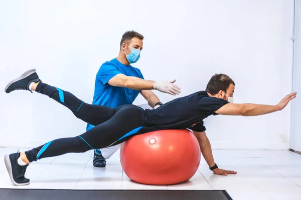 Fisioterapeuta Con Máscara Paciente Estirándose Sobre Una Pelota Fisioterapia Con —  Fotos de Stock