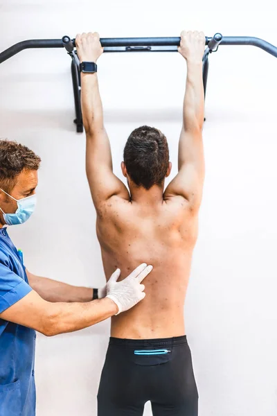 Physiotherapist with mask with his hand on the back of a patient in a dominated. Physiotherapy with protective measures for the Coronavirus pandemic, COVID-19. Osteopathy, sports chiromassage