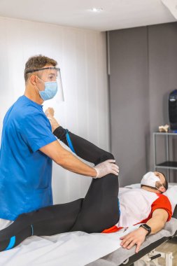 Bir hastayla çalışan maskeli bir fizyoterapist. Koronavirüs salgını için koruyucu önlemlerle fizik tedavi, COVID-19. Osteopati, tedavi edici kiromasaj.