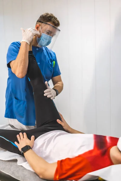 Egy Fizioterapeuta Maszkkal Képernyővel Aki Páciens Lábait Nyújtja Konzultáción Fizioterápia — Stock Fotó