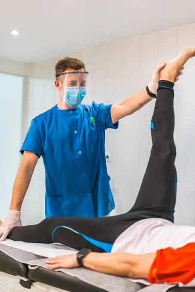 Fisioterapeuta Con Máscara Pantalla Que Estira Las Piernas Paciente Fisioterapia —  Fotos de Stock