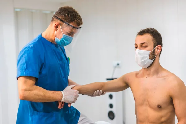 口罩带口罩的理疗师 为戴口罩的病人提供腕部按摩对Coronavirus大流行病Covid 19采取保护措施的理疗 治疗性脊椎按摩 — 图库照片