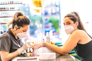 Kafkasyalı esmer müşteriye yüz maskeli Latin kız tırnaklarını boyuyor. Korod-19 salgınından sonra tekrar açılıyor. Manikür ve Pedikür Salonu. Coronavirüs
