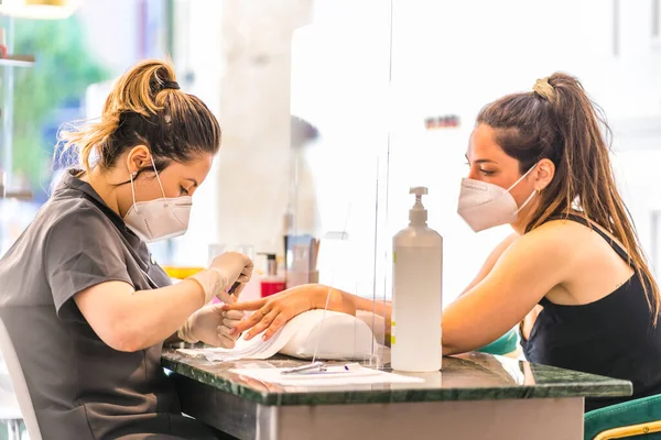 A manicure and pedicure salon worker with security measures and face masks. The reopening due to the covid-19 pandemic. Coronavirus