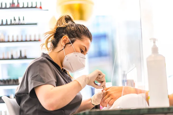 Pedicure treatment of a young Latina worker in the manicure and pedicure salon with safety measures and face masks. The reopening due to the covid-19 pandemic. Coronavirus