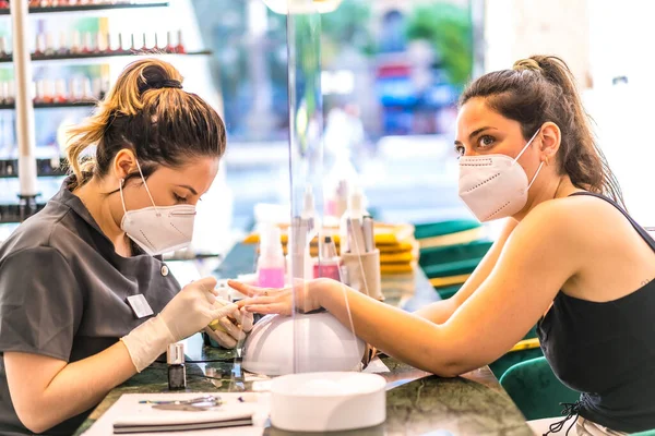 美容美发美容院的工作人员 戴着面罩 在白种人客户上画着五颜六色的指甲 Corod 19大流行病后重新开放 美容院和美容院Coronavirus 免版税图库图片