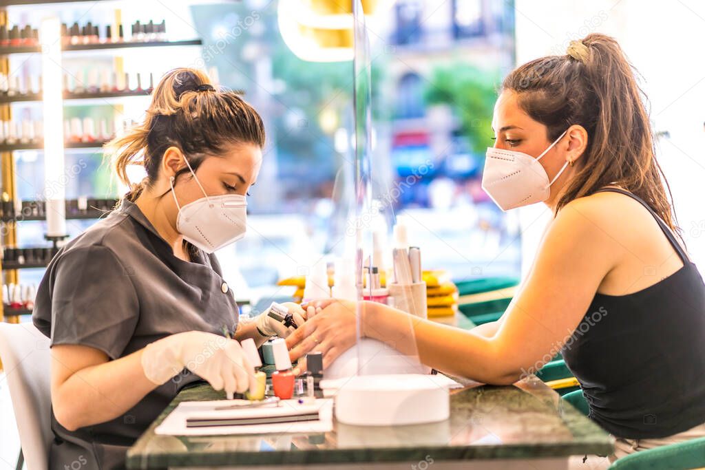 A worker with security measures and a face mask working with a client. Reopening after the coronavirus pandemic. Manicure and Pedicure Salon.