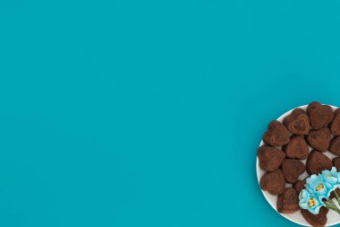 Mavi arka planda beyaz kasede kalp şeklinde çikolatalar ve mavi çiçekler. Sevgililer Günü konsepti. Sevgililer Günü tebrik kartı. Kopya alanı ile düz uzanma biçimi.