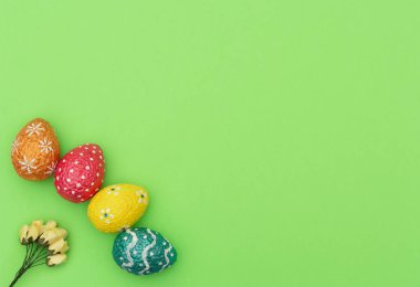 Renkli turuncu, mavi, kırmızı ve sarı paskalya yumurtaları yeşil arka planda sarı bahar çiçekleri. Mutlu Paskalya tatili konsepti. Kopya alanı ile düz uzanma biçimi.