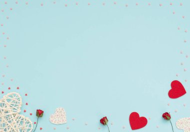 Sevgililer Günü 'nün mavi arka planında rattan ve keçeli kalpler, kırmızı güller ve küçük kırmızı ve pembe kalpler var. Selamlar, davetiye. Düğün, aşk, mutluluk konsepti. Düz konum, kopyalama alanı olan üst görünüm.