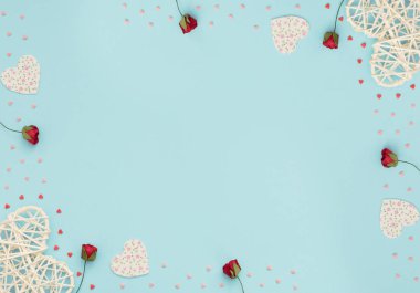 Sevgililer Günü 'nün mavi arka planında rattan ve keçeli kalpler, kırmızı güller ve küçük kırmızı ve pembe kalpler var. Selamlar, davetiye. Düğün, aşk, mutluluk konsepti. Düz konum, kopyalama alanı olan üst görünüm.