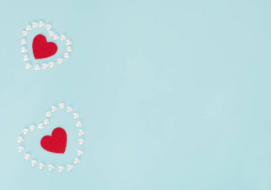 Mavi arka planda küçük inci kalplerden yapılmış kalplerin içinde iki kırmızı keçeli kalp. Sevgililer Günü, düğün, aşk, mutluluk konsepti. Tebrik kartı ya da davetiye. Kopya alanı ile düz uzanma biçimi.