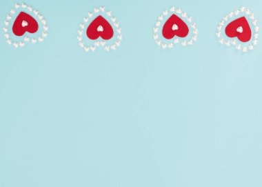 Mavi arka planda küçük inci kalplerden yapılmış dört kırmızı keçeli kalp. Sevgililer Günü, düğün, aşk, mutluluk konsepti. Tebrik kartı ya da davetiye. Kopya alanı ile düz uzanma biçimi.