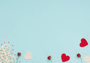 Sevgililer Günü 'nün mavi arka planında rattan ve keçeli kalpler, kırmızı güller ve küçük kırmızı ve pembe kalpler var. Selamlar, davetiye. Düğün, aşk, mutluluk konsepti. Düz konum, kopyalama alanı olan üst görünüm.