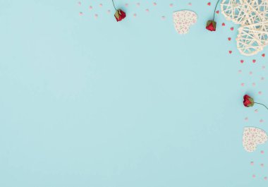 Sevgililer Günü 'nün mavi arka planında rattan ve keçeli kalpler, kırmızı güller ve küçük kırmızı ve pembe kalpler var. Selamlar, davetiye. Düğün, aşk, mutluluk konsepti. Düz konum, kopyalama alanı olan üst görünüm.