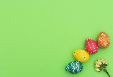 Renkli turuncu, mavi, kırmızı ve sarı paskalya yumurtaları yeşil arka planda sarı bahar çiçekleri. Mutlu Paskalya tatili konsepti. Kopya alanı ile düz uzanma biçimi.