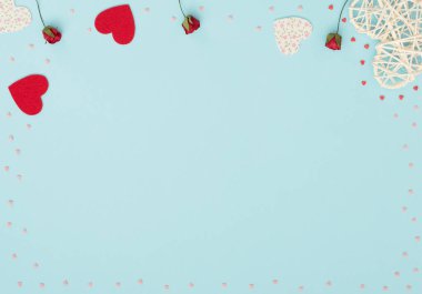 Sevgililer Günü 'nün mavi arka planında rattan ve keçeli kalpler, kırmızı güller ve küçük kırmızı ve pembe kalpler var. Selamlar, davetiye. Düğün, aşk, mutluluk konsepti. Düz konum, kopyalama alanı olan üst görünüm.