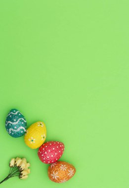Renkli turuncu, mavi, kırmızı ve sarı paskalya yumurtaları yeşil arka planda sarı bahar çiçekleri. Mutlu Paskalya tatili konsepti. Kopya alanı ile düz uzanma biçimi.