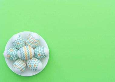 Süslü Paskalya yumurtaları yeşil arka plandaki beyaz tabakta yatar. Mutlu Paskalyalar ve bahar tatili. Selamlar, davetiye. Kopya alanı ile düz uzanma biçimi.