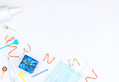 Beyaz arka plan, paketlenmiş hediye kutusu, flamalar, mumlar, tıbbi maske, termometre ve dezenfektan. Sosyal mesafe, doğum günü, parti, tecrit, karantina, COVID-19 konsepti. Düzleştirme biçimi. 