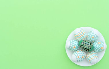 Süslü Paskalya yumurtası yeşil arka plandaki beyaz tabakta yatıyor. Mutlu Paskalya tatili konsepti. Selamlar, davetiye. Kopya alanı ile düz uzanma biçimi.