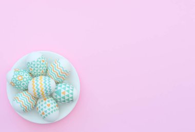 Süslü Paskalya yumurtası pembe arka plandaki beyaz tabakta yatıyor. Mutlu Paskalya tatili konsepti. Selamlar, davetiye. Kopya alanı ile düz uzanma biçimi.