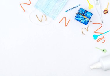 Beyaz arka plan, paketlenmiş hediye kutusu, flamalar, mumlar, tıbbi maske, termometre ve dezenfektan. Sosyal mesafe, doğum günü, parti, tecrit, karantina, COVID-19 konsepti. Düzleştirme biçimi. 