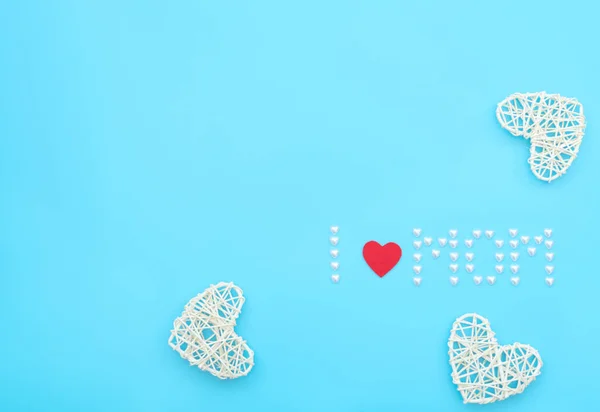 The text I love mom made of small pearl hearts with red felt heart and rattan hearts on blue background. Mothers day, Birthday or other suitable event celebration card concept. Flat lay, copy space
