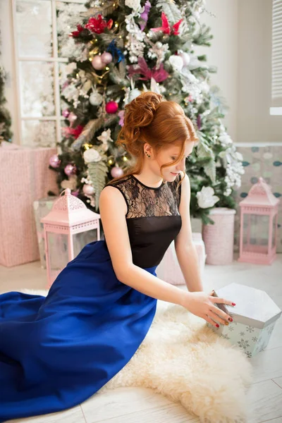 Una chica en un vestido de noche abre un regalo para el nuevo año. Nochevieja. Navidad . —  Fotos de Stock