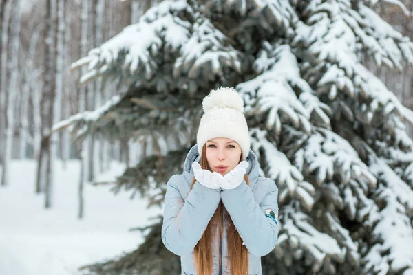 一个女孩穿着暖和的冬天的衣服和帽子吹雪在冬天森林里，水平 — 图库照片