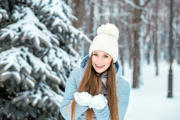 Een meisje gekleed in warme winterkleren en een hoed poseren in een winter forest. Model met een mooie glimlach in de buurt van de kerstboom. — Stockfoto
