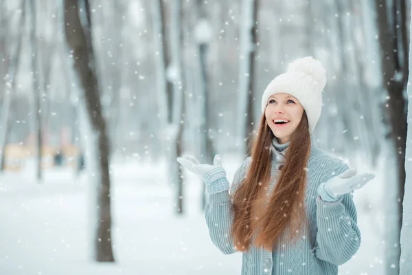 Outdoor close-up portrait of young beautiful happy smiling girl, wearing stylish knitted winter hat and gloves. Model expressing joy Day light. Magic snowfall effect. Toned — Stock Photo, Image