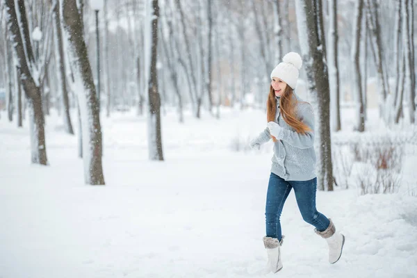 户外特写照片, 年轻漂亮的笑脸女郎, 身穿时尚针织冬帽和手套。一个女孩在白雪覆盖的森林里奔跑. — 图库照片