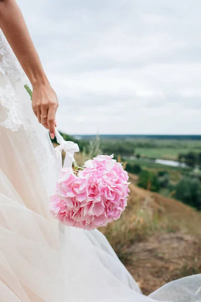 Μέρη του σώματος. Στο χέρι του ένα νεαρό κορίτσι, μια νύφη σε ένα γαμήλιο φόρεμα. Κατέχει ένα λουλούδι από ένα ροζ Ορτανσία. — Φωτογραφία Αρχείου
